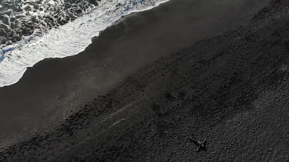 Aerial Shot of Man Relaxing on the Black Sand of a Beach.