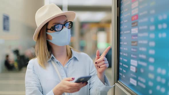 Traveler Is Casual Outfit and Face Mask Searching Flight on Timetable in Airport alt