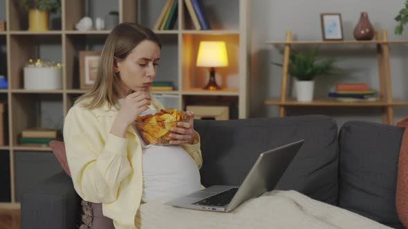 Pregnant Lady Having Snack While Using Laptop at Home alt