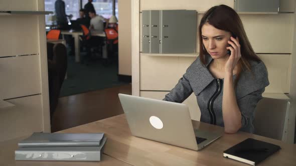 Businesswoman Working on the Laptop and Talking By the Cellphone in the Separated Office alt