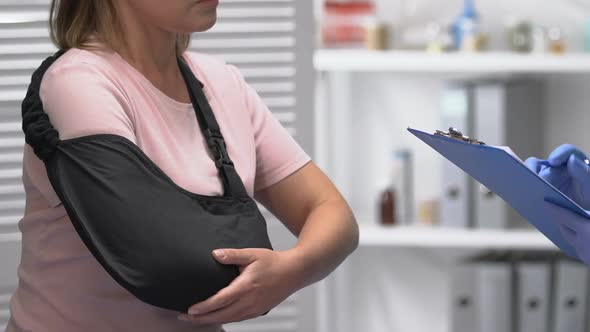 Traumatologist Consulting Lady Patient in Arm Sling, Writing Examination Result