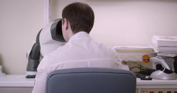 The Man Sits with His Back and Looks Into the Microscope alt