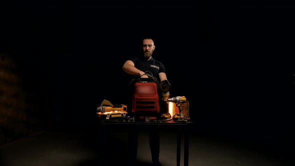 Young engineer with a beard collects tools in a special bag on a black background