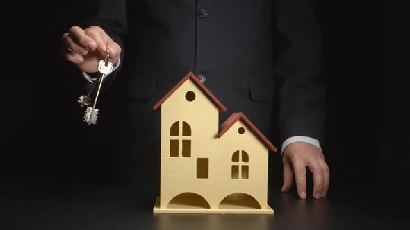 Businessman shakes a keys in his hand near a house model