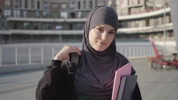Beautiful Muslim Woman in Hijab Posing with Books Outdoors on Sunny Day. Portrait of Charming Middle alt