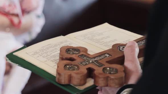 Priest in a black cassock reads a prayer holding a bible with a cross in his hand