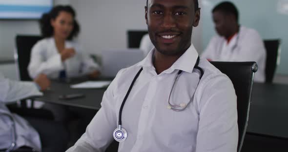 Portrait of african american male doctor sitting in meeting room looking to camera smiling alt