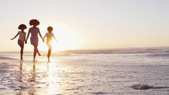 African american mother son and daughter having fun walking together during sunset on the beach alt