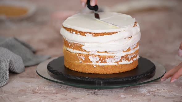 Woman's hand spreading whipped white cream on sponge layer cake.