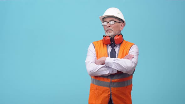 Adult engineer in a helmet, glasses and a protective vest with headphones confidently crosses arms alt