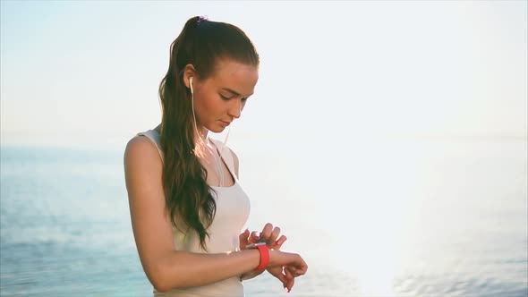 Young Woman Using Smart Watches in Front of the Sea During Sunset alt