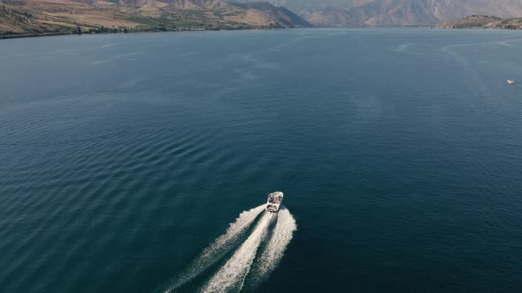 Pristine Blue Lake Water With Drone Following Motorboat Cruising In Desert Environment alt