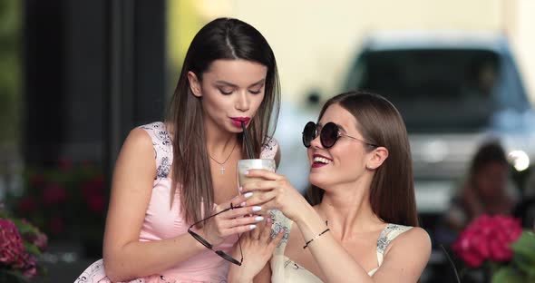 Two Beautiful Girls Drinks Coffee in the Summer Cafe and They Are Surprised