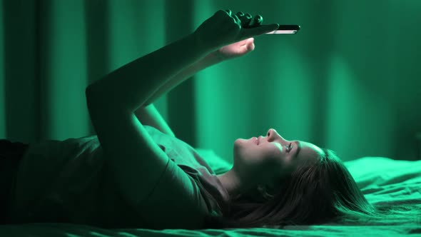 Young Woman Browsing Smartphone Watching Social Media Lying in Bed Side View