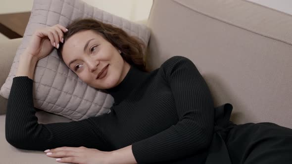 A Happy Woman Lying on a Sofa on a Pillow Enjoying a Rest in a Bright Room alt