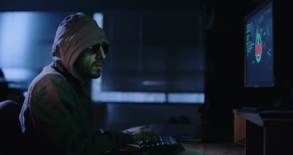 Computer hacker sitting in a dark room hacking security systems alt