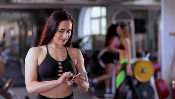 A Beautiful Athletic Woman a Woman in the Gym Holds a Phone in Her Hand and Types a Message Then