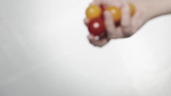 Person Throws Red and Yellow Cherry Tomatoes Into Water alt