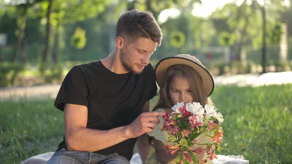 Little Girl Admiring Bouquet of Flowers Sitting with Young Man Outdoors in Sunbeam