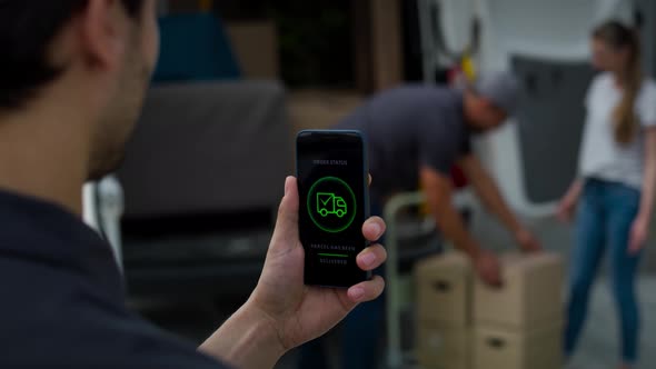 Rear view of delivery man holding phone with mobile app. Shot with RED helium camera in 8K. alt