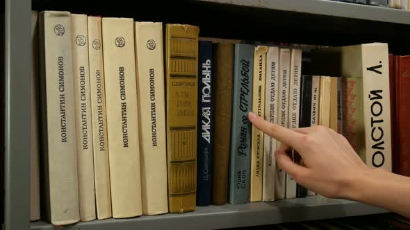 A Girl Chooses A Book From The Shelf In The Library