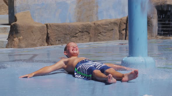 Boy laying down and getting splashed at fountain on summer day, slow motion alt