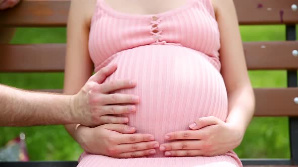 Close Up of Pregnant Woman Hands Stroking Belly on a Park Bench in the Summer alt