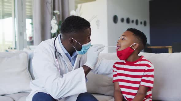 African american doctor wearing face mask taking a throat swab sample of boy at home alt
