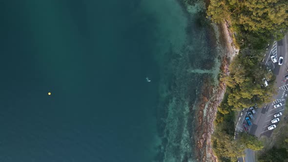 Static high drone view looking down on a coastal headland next to a carpark and road with scuba dive alt