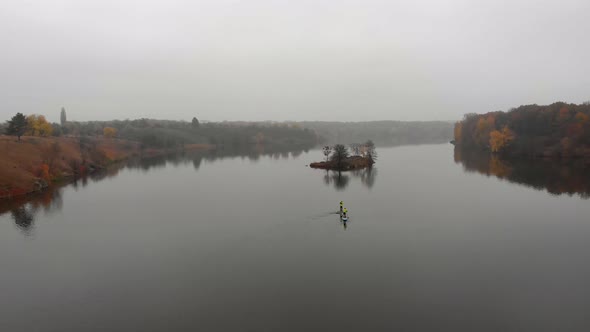 Man and Woman on Sup Paddle Boards at Wide River with Small Island on Golden Autumn Forest alt