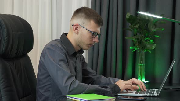 Concentrated focused man is working on computer, typing on keyboard, looking at screeen alt
