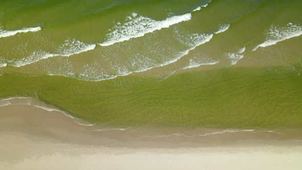 Slowly moving from baltic green seawater foamy waves towards the empty white-sand beach in Osetnik, alt