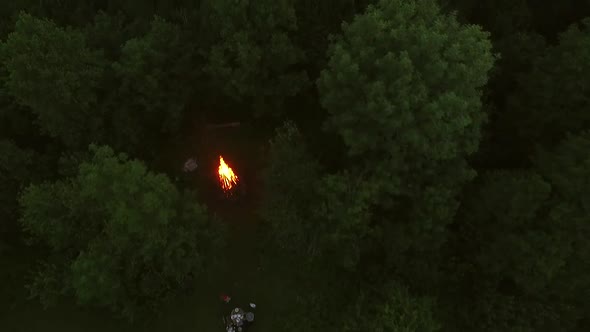 Aerial view of friend eating close to campfire in forest. alt
