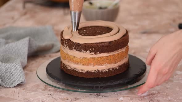 Chef's hands squeezing cream on rotating biscuit cake layers using confectionery bag.