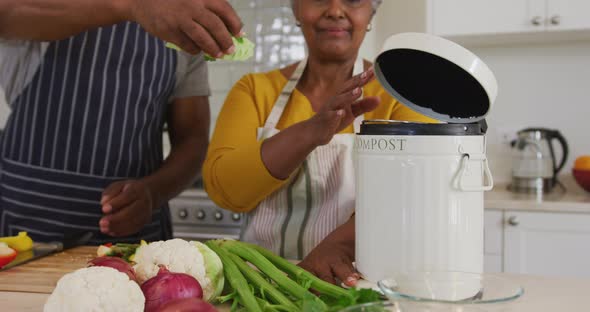 African american senior couple putting chopped vegetables in a tiffin box in the kitchen at home alt