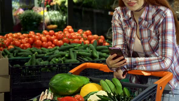 Girl Uses Smartphone at the Hypermarket alt