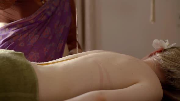 Young Female Patient Is Lying on Couch and Relaxing, Indian Masseuse Is Pouring Oil on Her Spinal alt