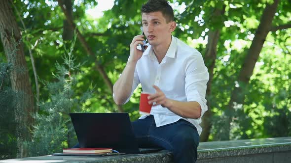 Trader Man Sitting In Park And Talking On Mobile Phone.