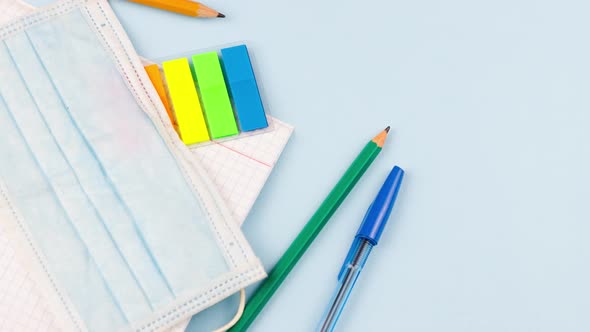 School Supplies with a Notepad Lie on a Pastel Blue Background with a Medical Mask alt