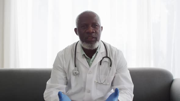 Portrait of male african american doctor wearing surgical gloves talking while having a videocall alt
