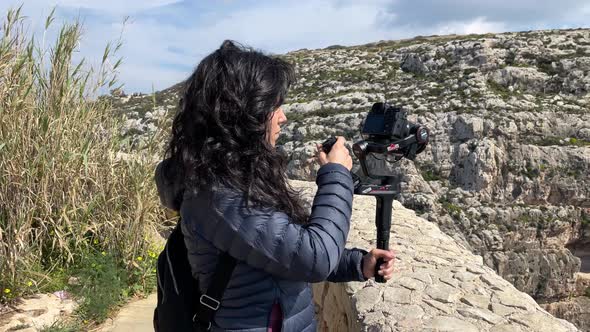 Young woman filming with her camera greats during an outdoor adventure with rocky landscape in the b alt