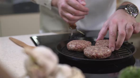 Chef roasting fat meat cutlet for hamburger on a metal grill frying pan. alt