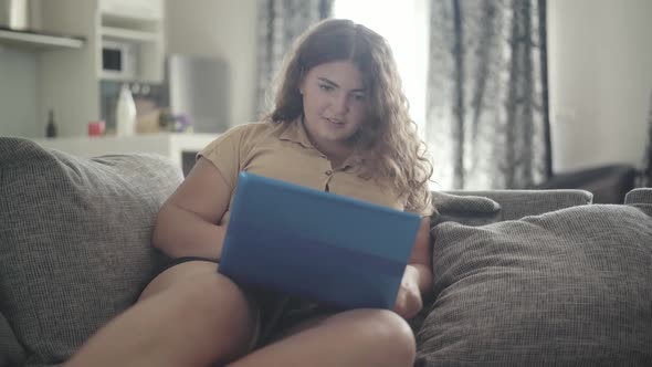 Portrait of Cheerful Plump Woman Using Social Media on Laptop and Smiling. Young Overweight alt