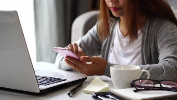 Young woman sitting at living room and working on laptop and smartphone at home alt