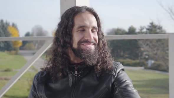 Portrait of Positive Hippie Man with Long Curly Hair and Beard Looking Away, Talking and Smiling alt