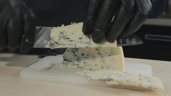 a Chef in Black Gloves with a Large Knife Cuts Dor Blue Cheese Into Pieces