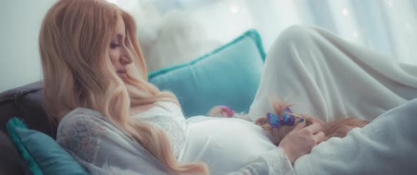 Beautiful pregnant woman petting her small terrier twin puppies on a cozy couch at home.  alt