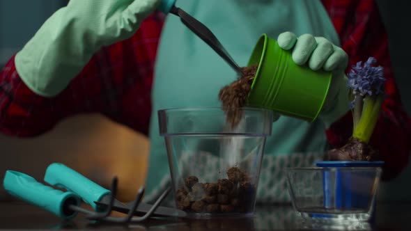 Female hand in glove taking pot with ground and throwing it to transparent flower pot