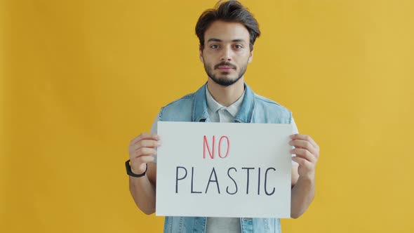 Slow Motion Portrait of Young Arab Man Holding No Plastic Banner on Yellow Background alt