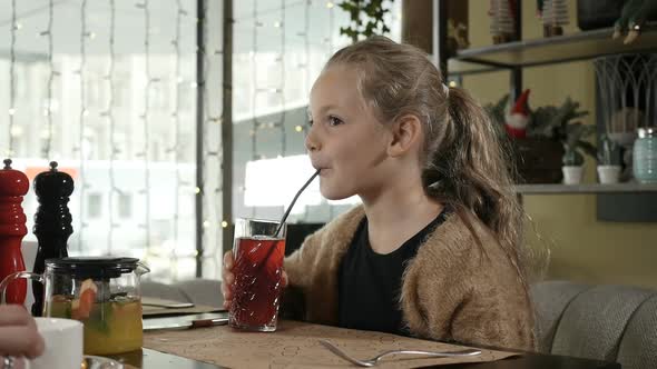 a Little Girl with Blonde Hair Sitting in a Restaurant Drinking Juice